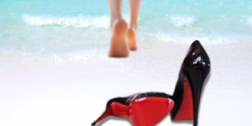 Red soled shoes in the sand with woman walking into the ocean.