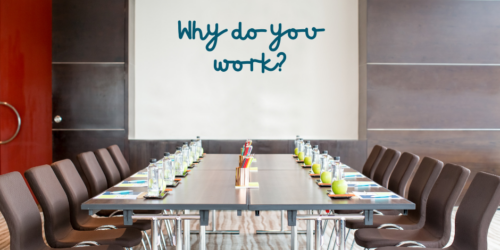 Company boardroom table with whiteboard with the questions Why do you work? handwritten.