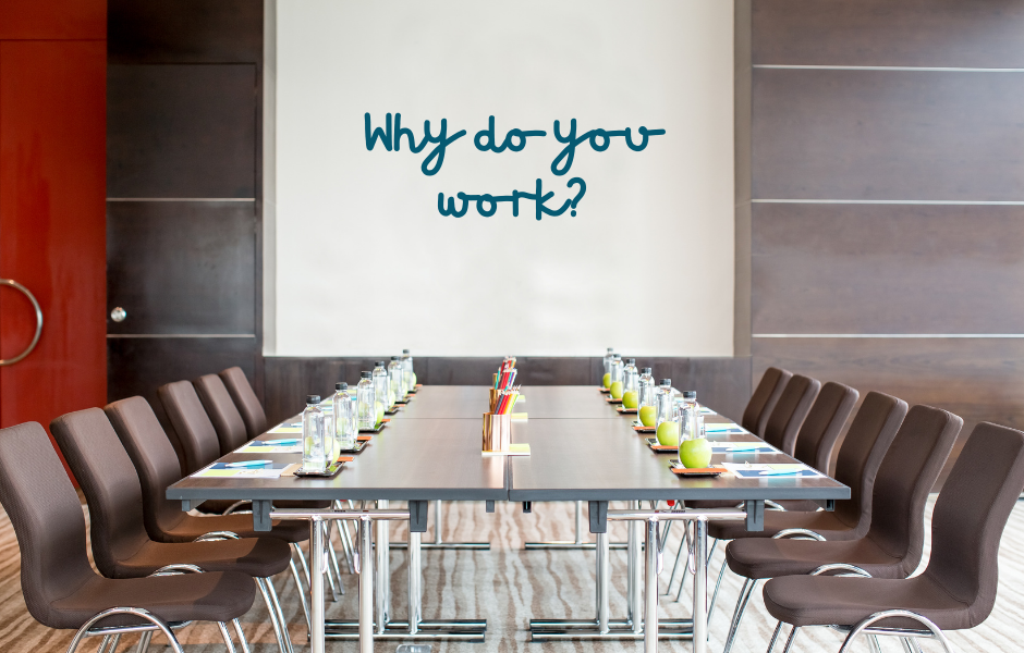 Company boardroom table with whiteboard with the questions Why do you work? handwritten.