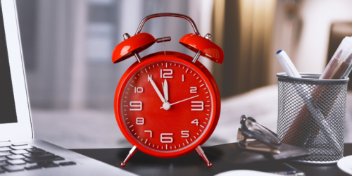 Red alarm clock on a professional desk between a computer and pens