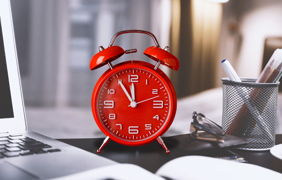 Red alarm clock on a professional desk between a computer and pens