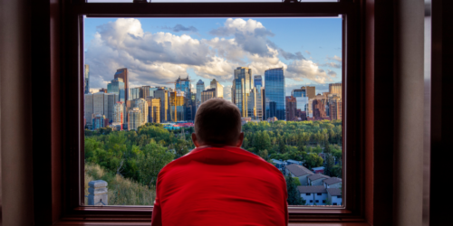 Man in red shirt staring out his window at downtown calgary