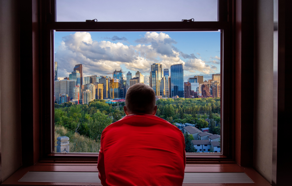 Man in red shirt staring out his window at downtown calgary